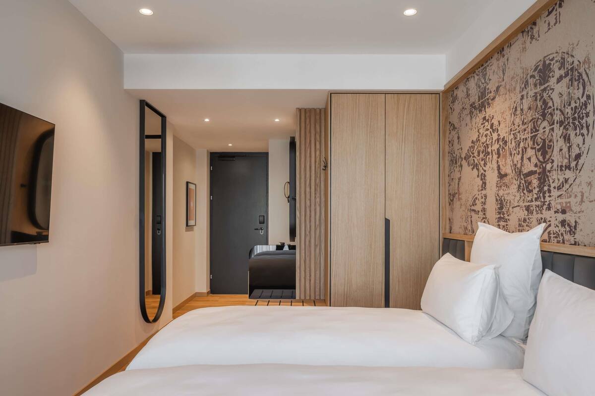 Une chambre d’hôtel moderne dotée d’un grand lit, d’un miroir, d’une armoire et donnant sur la chambre adjacente.