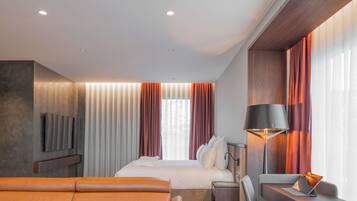 Una habitación de hotel moderna con una cama, un sofá, un escritorio con una computadora portátil, una lámpara y un televisor montado en la pared.