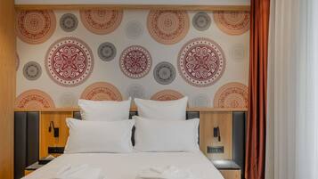 Une chambre d’hôtel comprenant un lit, des oreillers, une table de chevet, une tête de lit en bois et un mur orné de motifs circulaires.