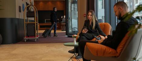 A modern hotel lobby with a reception desk, a luggage cart, and a seating area with a plant.