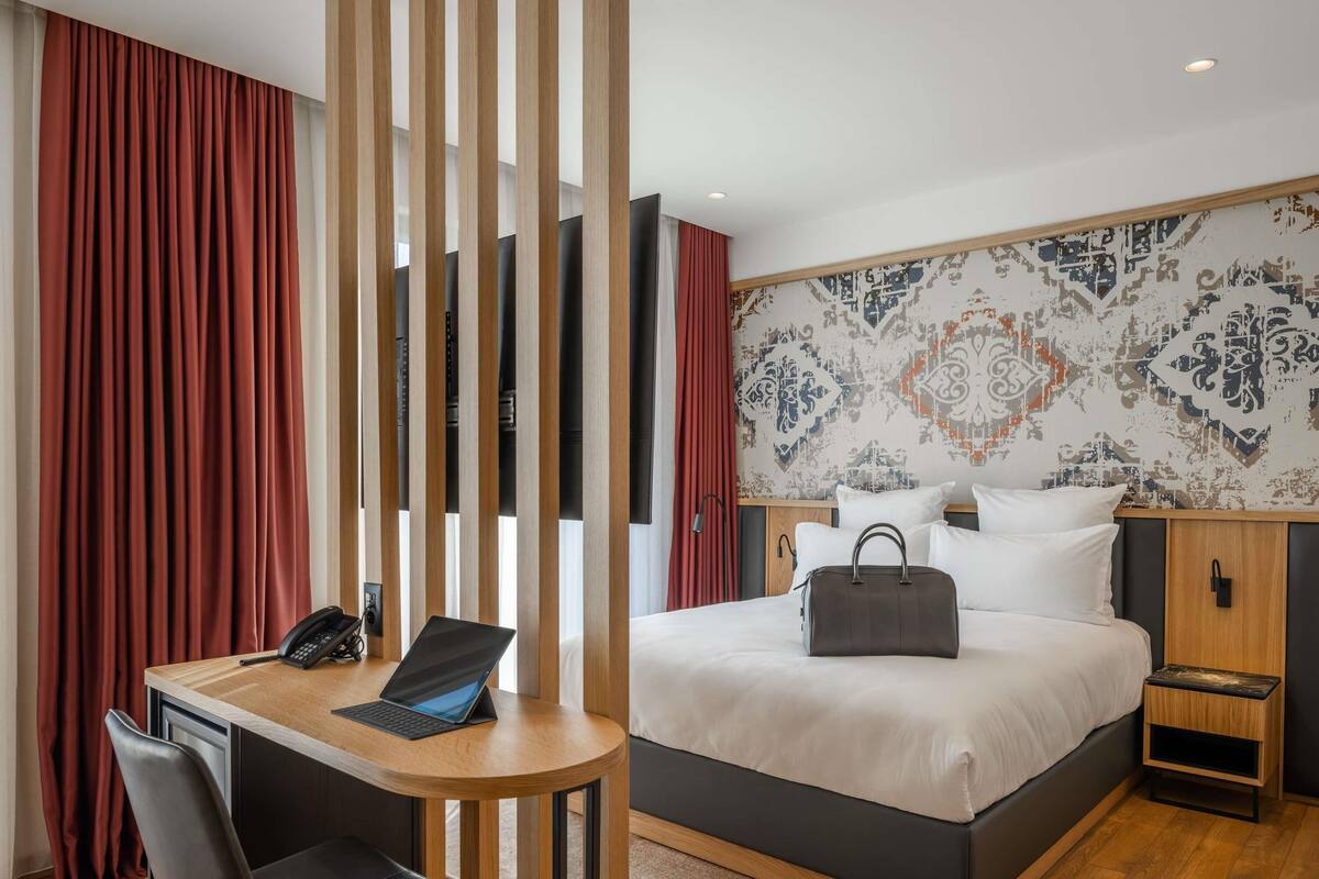 Une chambre d’hôtel équipée d’un lit, d’une table de chevet, d’un ordinateur portable, d’une chaise et d’un bureau avec un téléphone.