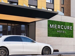 Un coche blanco estacionado frente al Hotel Mercure, con fachada moderna y una placa con el nombre del hotel.