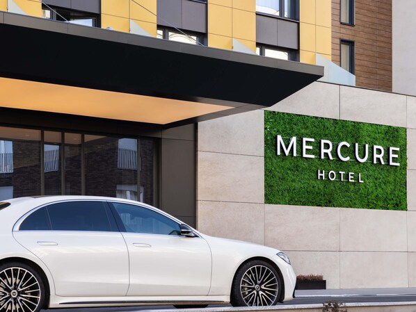 A white car parked in front of the Mercure Hotel, with a modern facade and a sign displaying the hotel name.