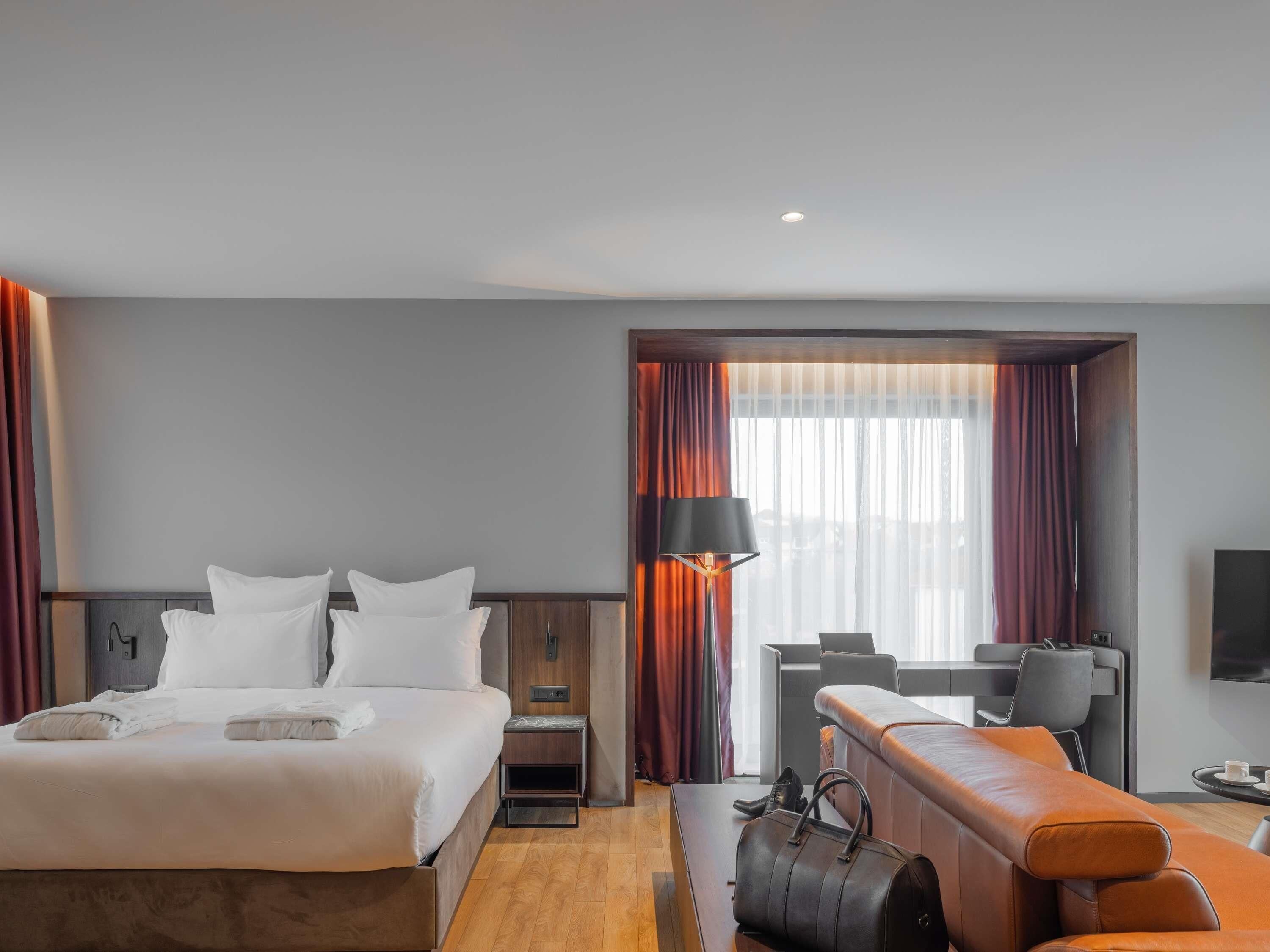 A hotel room with a bed, a desk, a chair, a sofa, and a television.