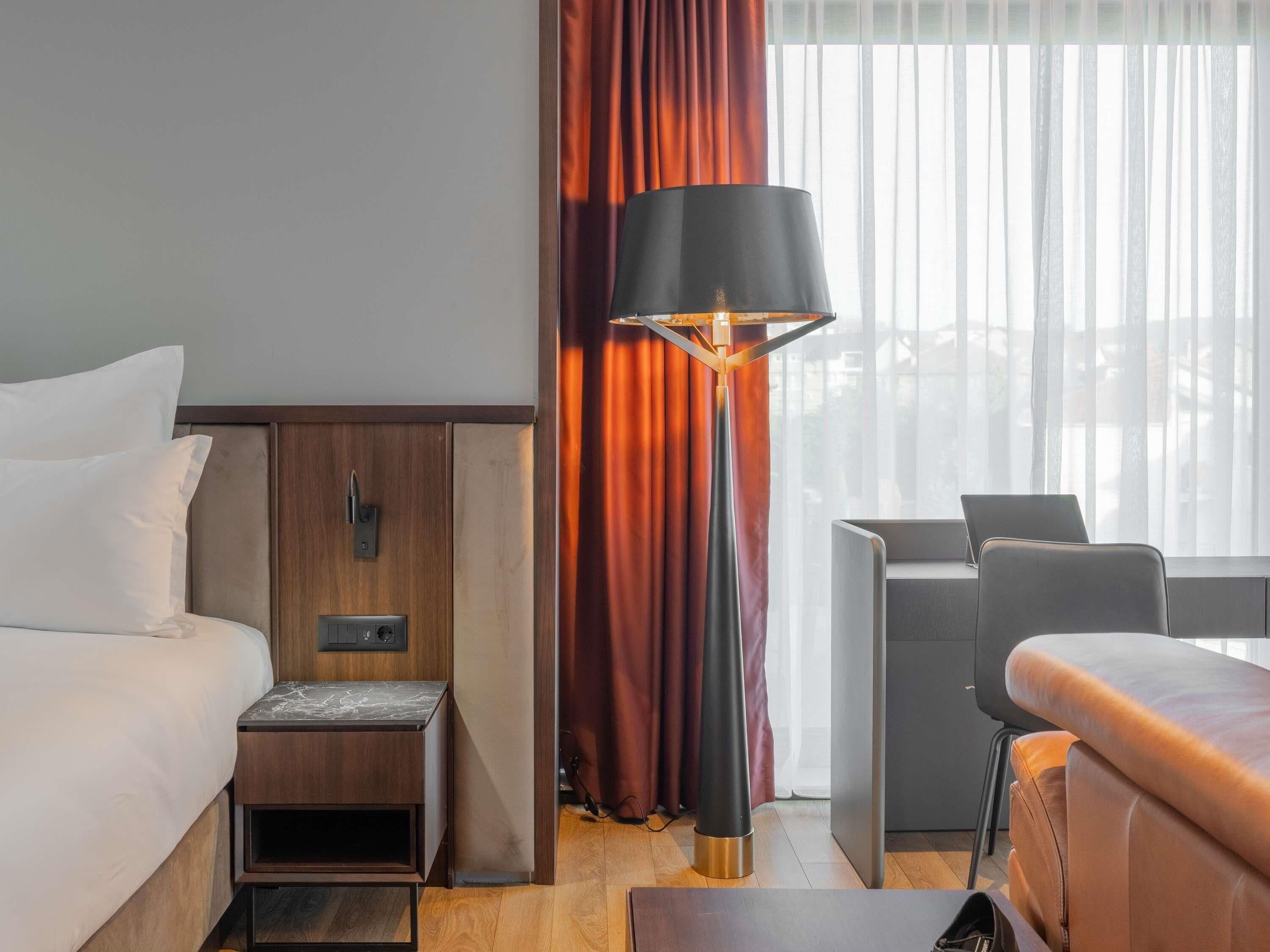A hotel room with a bed, bedside table, lamp, desk, and chair.