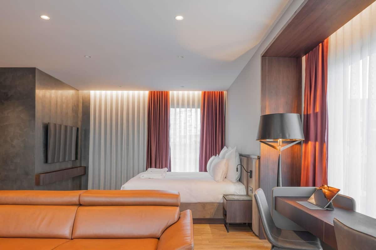 Ett modernt hotellrum med en säng, en sittgrupp, ett skrivbord med en bärbar dator och en tv som är monterad på väggen.
