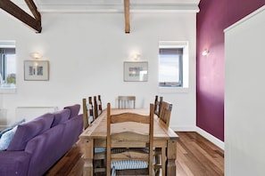 Un coin repas avec une table et des chaises en bois, un canapé violet et des tableaux encadrés accrochés aux murs.