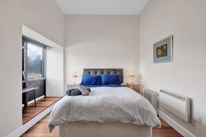 Une chambre à coucher avec un lit, des lampes de chevet, un radiateur, une fenêtre et un tableau au mur.
