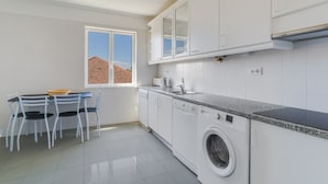 Una cucina compatta con mobili bianchi, una lavatrice e un'area pranzo con tavolo e sedie.