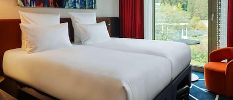 Ein Doppelbett mit weißen Leinen, ein roter Vorhang, ein großes abstraktes Gemälde und Blick auf Bäume durch ein Fenster.