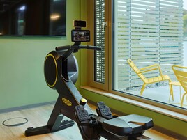 Uma bicicleta ergométrica com visor digital, posicionada perto de uma janela com persianas.