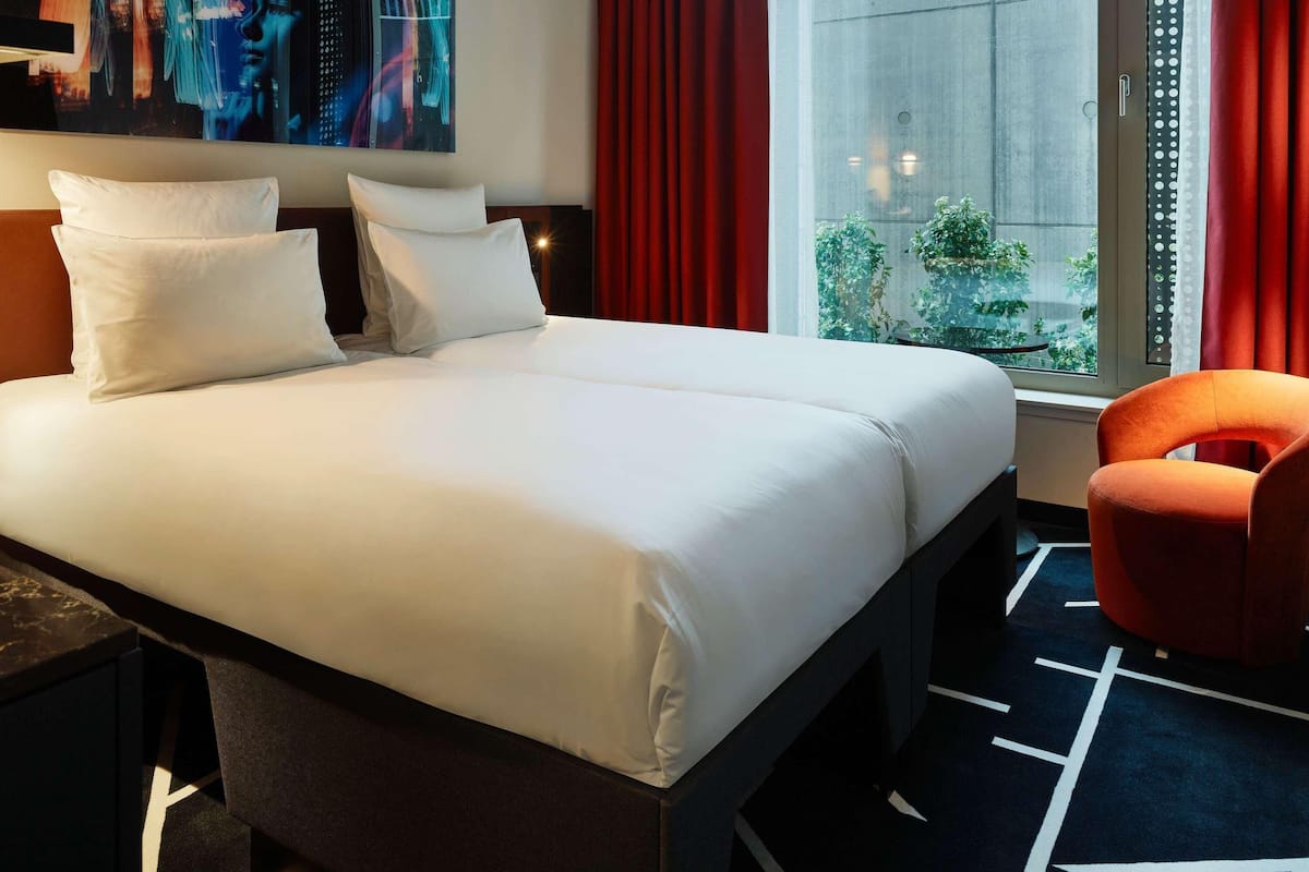 A hotel room with a bed, a chair, a window, and a painting on the wall.