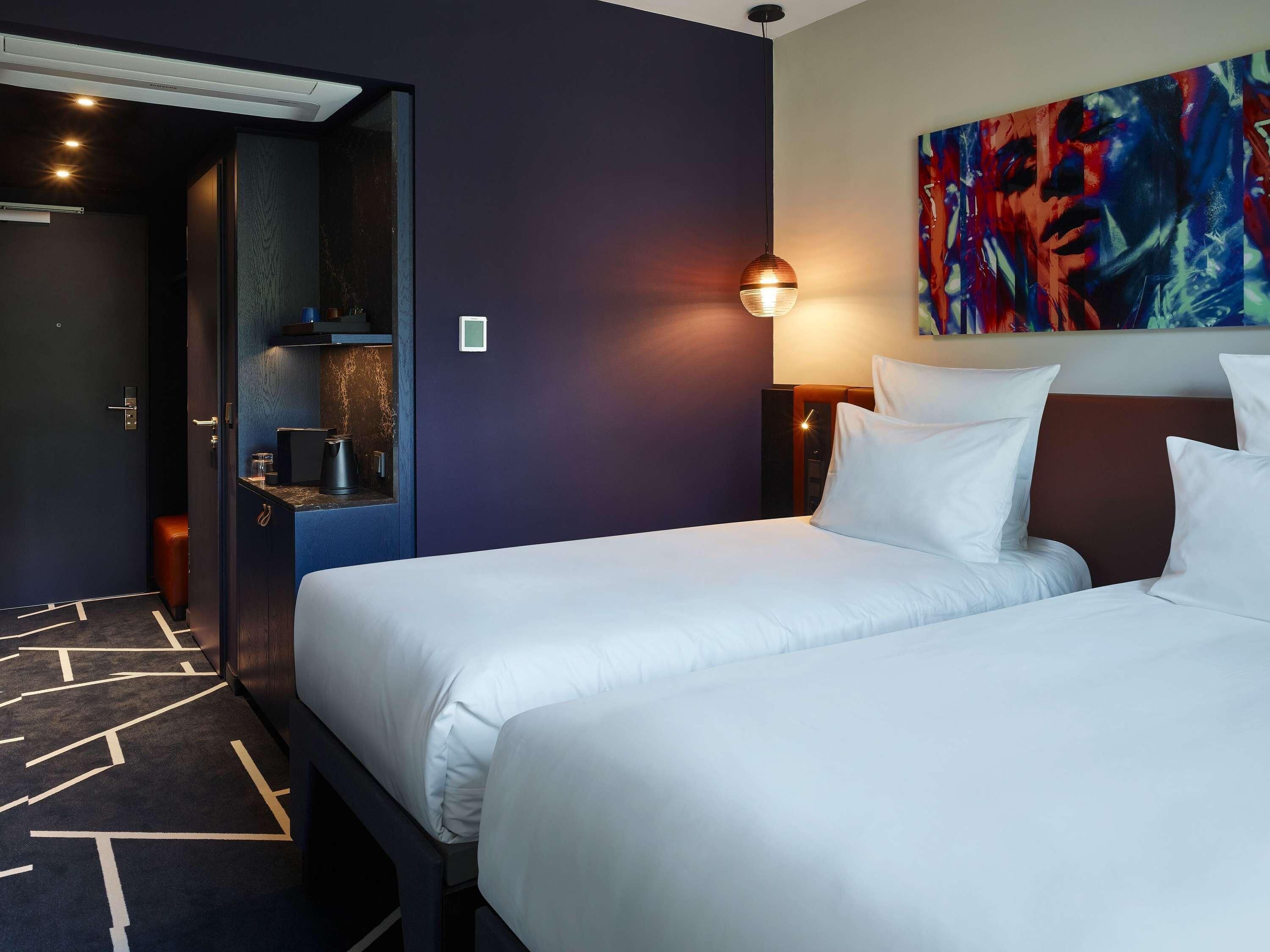 A hotel room with two beds, a painting on the wall, and a coffee machine.