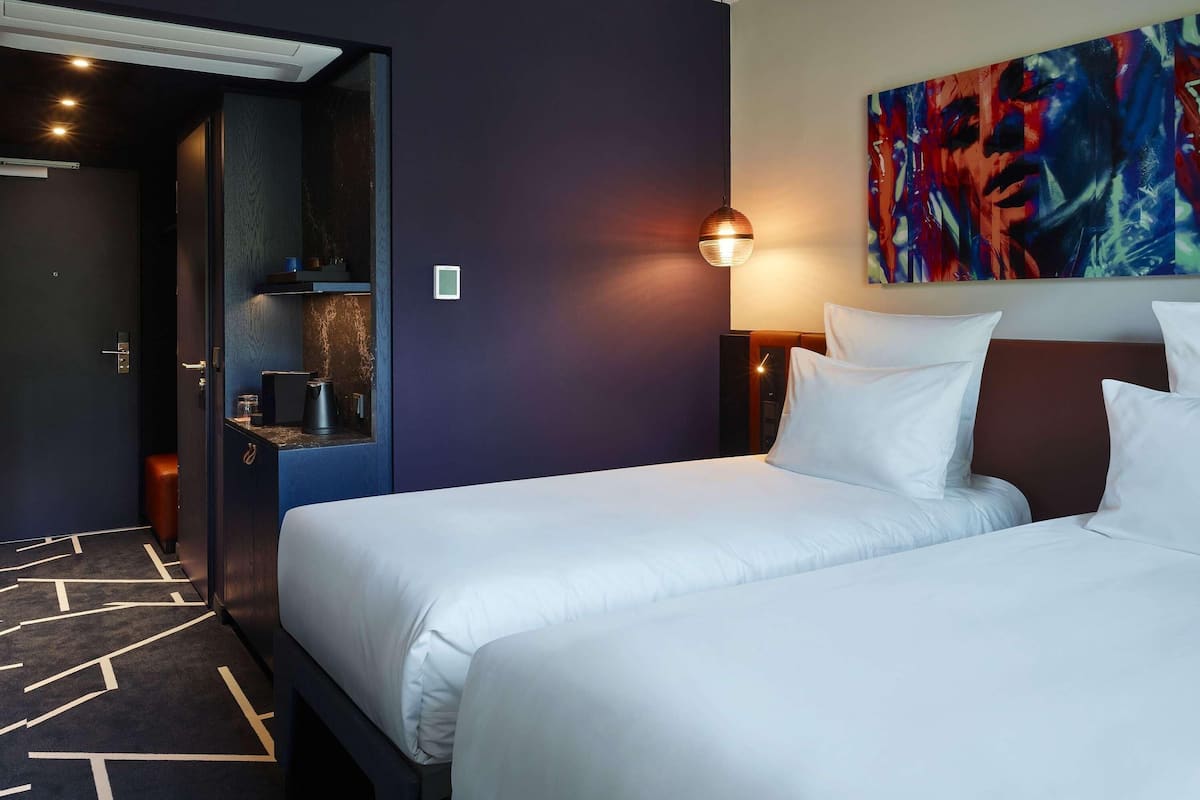 A hotel room with two beds, a painting on the wall, and a coffee machine.