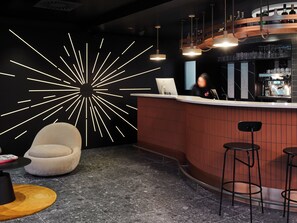 A modern bar area with a curved counter, bar stools, a round seating area, and a unique wall light design.