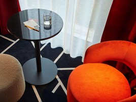 Una habitación con una mesa redonda, un vaso de agua, un bloc de notas y un bolígrafo. Hay dos sillas, una color beige y otra naranja.
