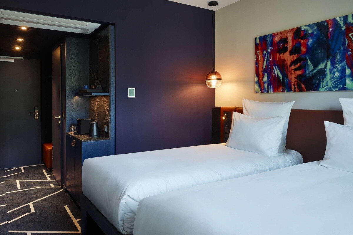 A hotel room with two beds, a painting on the wall, and a coffee machine.