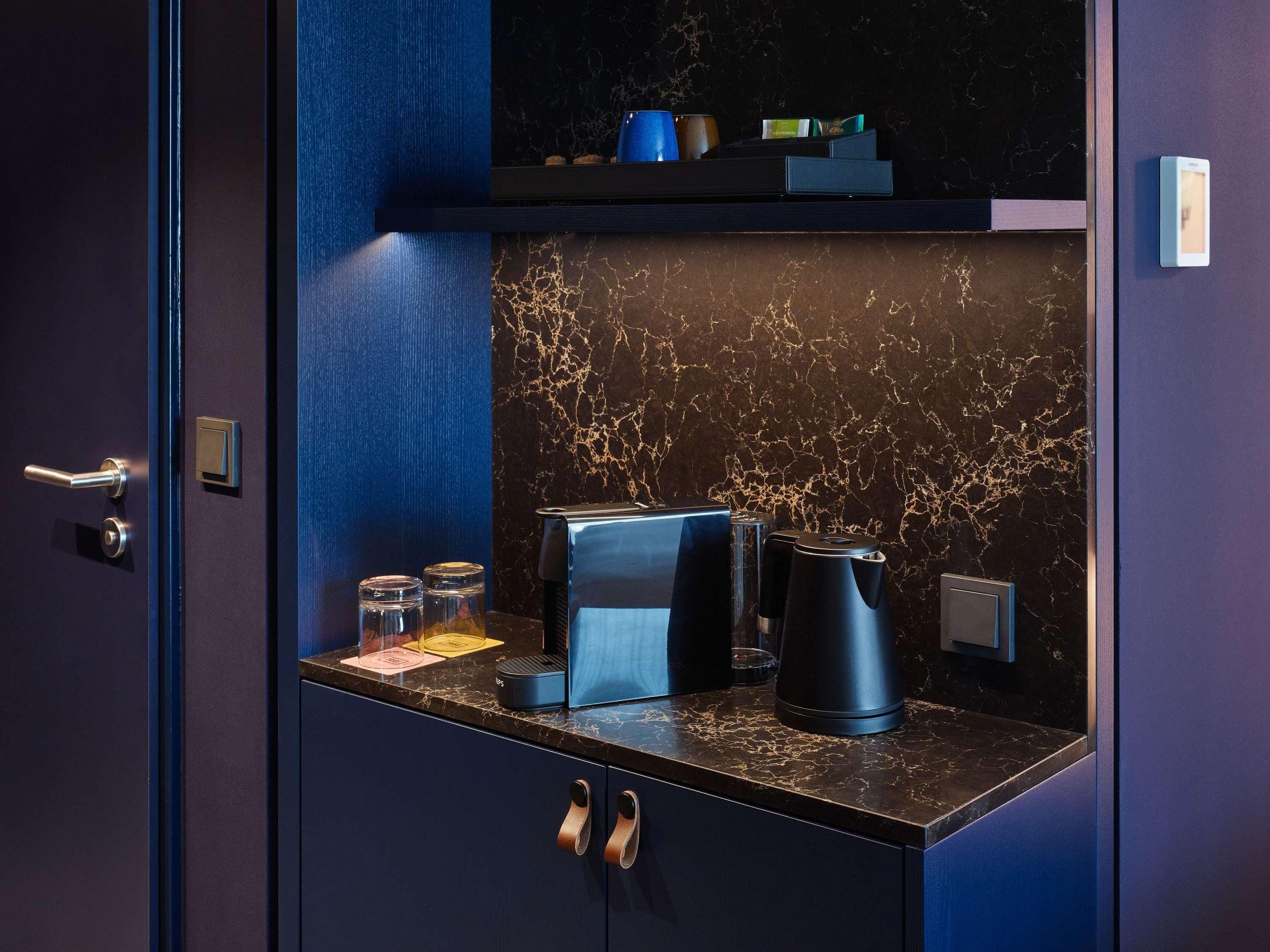 Una habitación azul oscuro con un salpicadero de mármol, una cafetera, un hervidor y un estante pequeño con objetos.