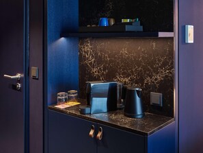 A dark blue room with a marble backsplash, a coffee maker, a kettle, and a small shelf with items. - Tribe Baden Baden (Baden-Baden)