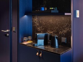 Una habitación azul oscuro con un salpicadero de mármol, una cafetera, un hervidor y un estante pequeño con objetos.