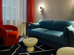 A modern living room with a blue sofa, a red chair, a small round table, and a wall-mounted light fixture.