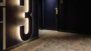 Un couloir avec un grand panneau lumineux affichant le chiffre « 3 », une porte dotée d’un clavier pour l’ouverture et des panneaux indicateurs indiquant les numéros des pièces.