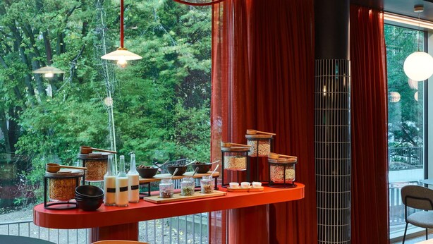 Un intérieur moderne avec un coin repas, des rideaux rouges et une vue sur la verdure environnante.