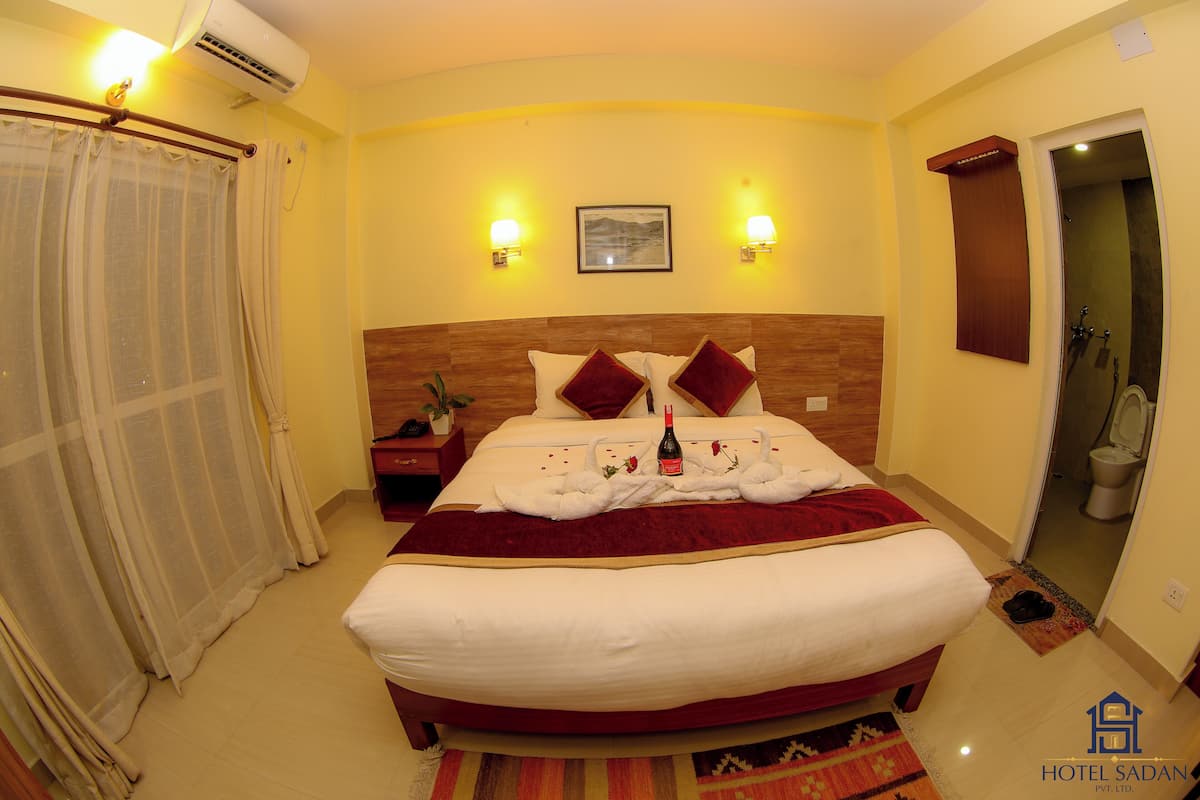 A hotel room with a large bed, a wooden headboard, two wall-mounted lamps, a framed picture, and a bathroom visible through an open door.