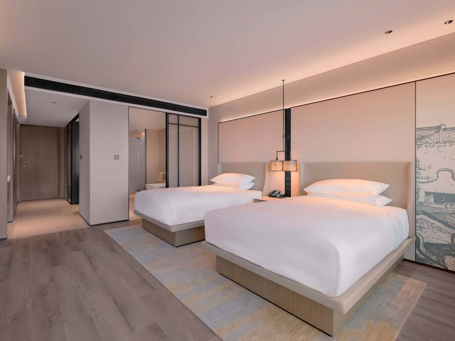 A modern hotel room with two beds, a large mirror, and a wall-mounted artwork.
