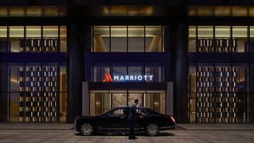 A black car parked in front of a Marriott hotel entrance with a person standing beside it.