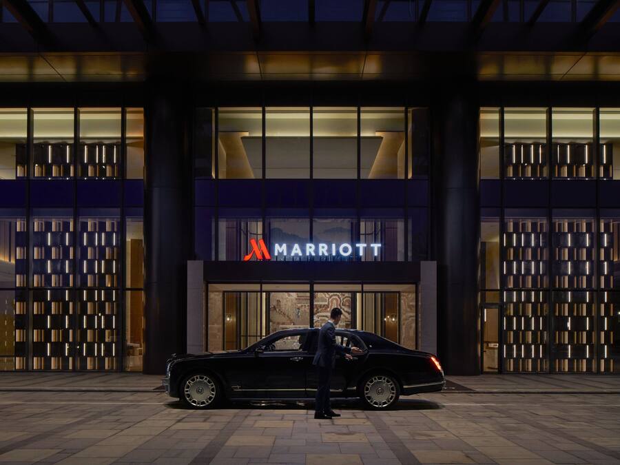 A black car parked in front of a Marriott hotel entrance with a person standing beside it.