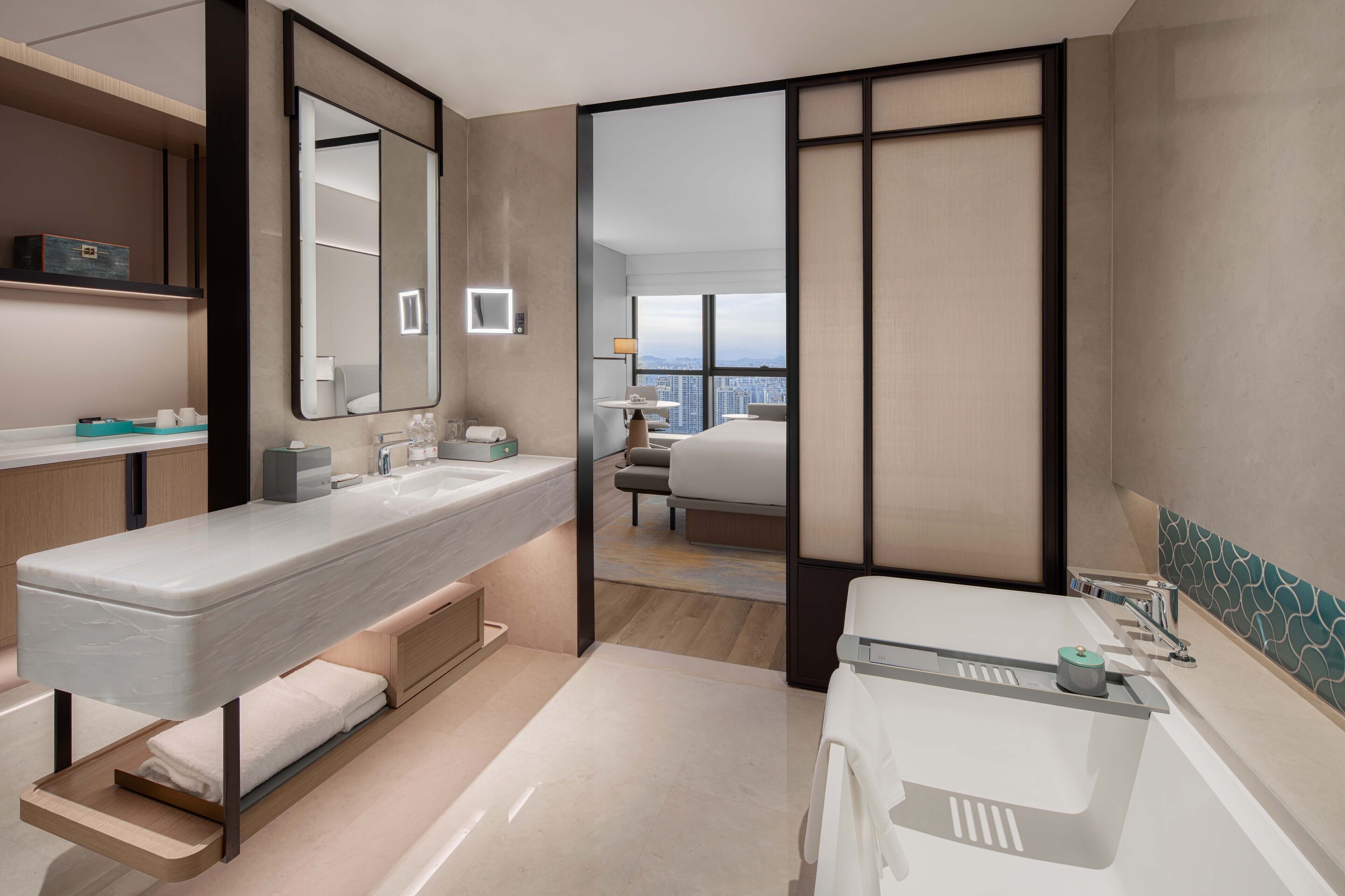 A modern hotel bathroom with a large mirror, dual sinks, and a view of the city through a large window.