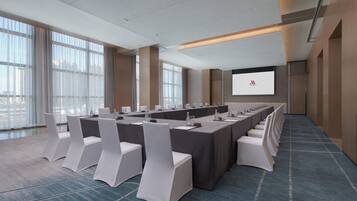 Un salón de conferencias con una larga mesa, sillas blancas y una pantalla para proyector.