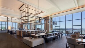 Un hall de hotel amplio y moderno con una zona de bar espaciosa, asientos cómodos y grandes ventanales que ofrecen vistas panorámicas de la ciudad.