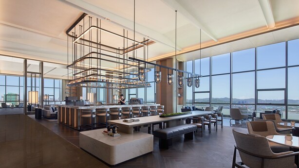 Un hall de hotel amplio y moderno con una zona de bar espaciosa, asientos cómodos y grandes ventanales que ofrecen vistas panorámicas de la ciudad.