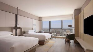 Una habitación de hotel moderna con dos camas, un escritorio, un televisor y un ventanal con vistas a la ciudad.