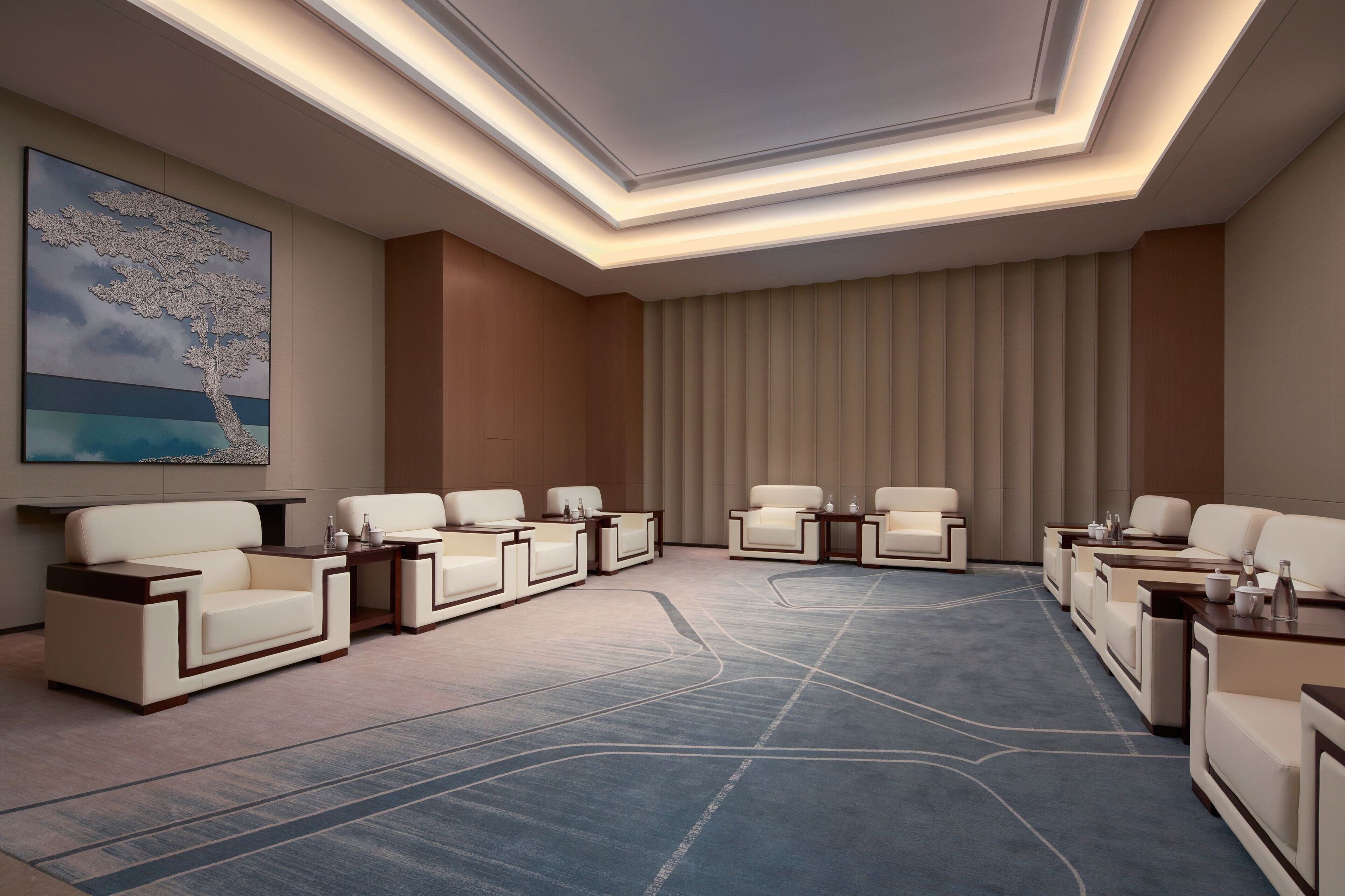 A modern conference room with a large, abstract painting, a patterned carpet, and a row of white leather chairs.