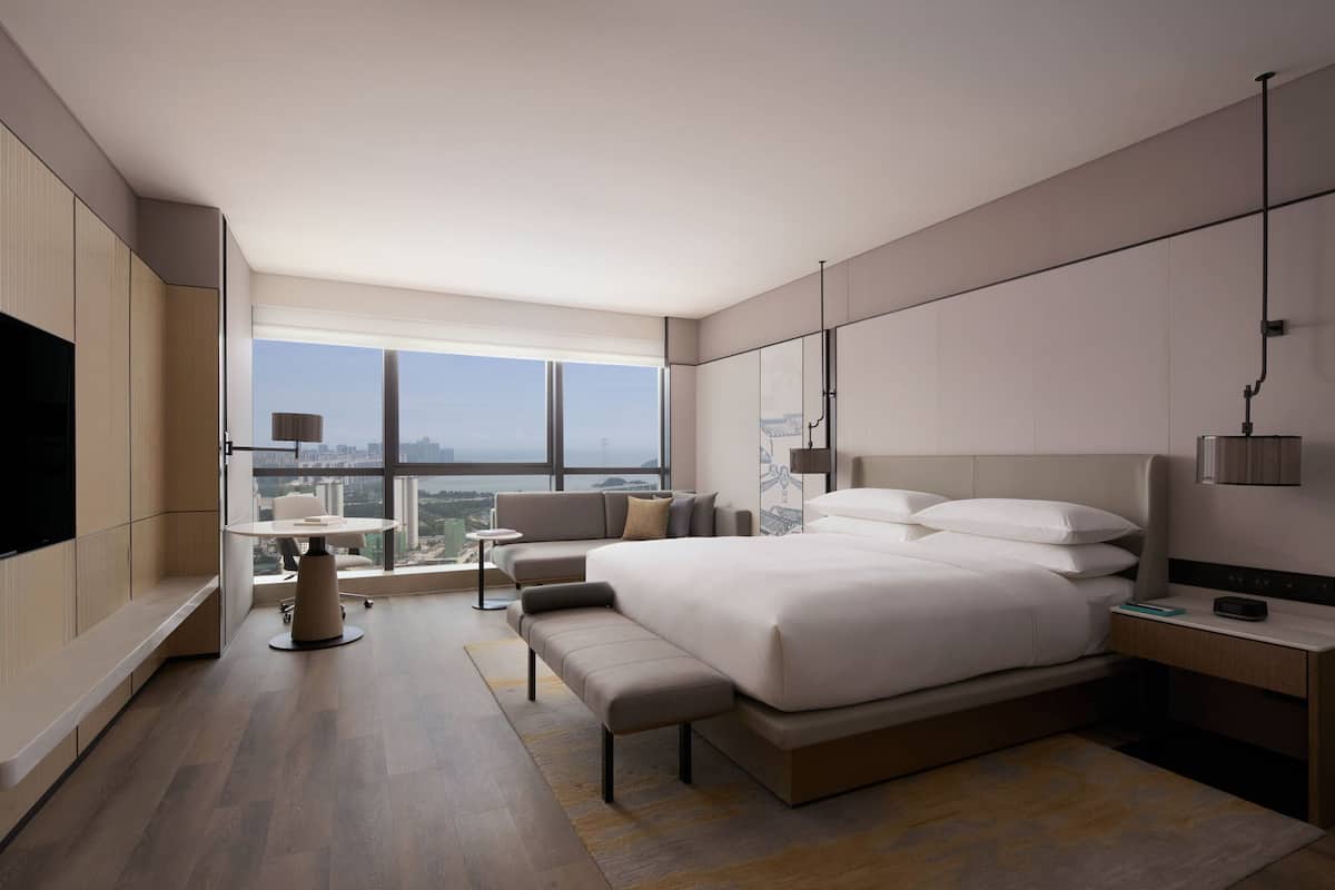 A modern hotel room with a large bed, a desk, a chair, and a TV.