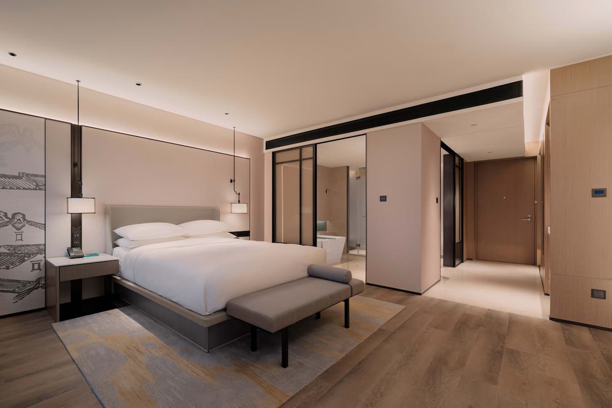 A modern hotel room with a large bed, bedside tables, a bench, and a walk-in closet.