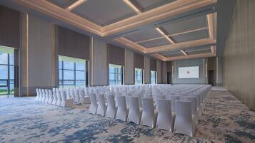 Un salón de conferencias con filas de sillas blancas, ventanas amplias y suelo alfombrado.