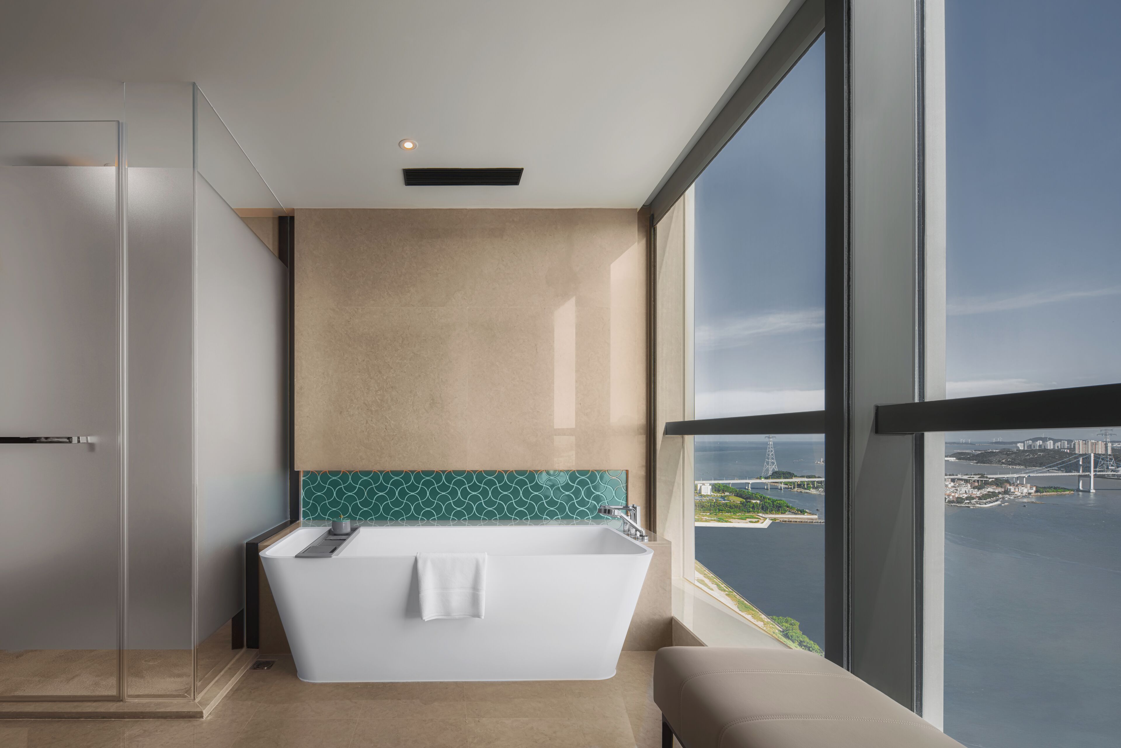 A modern bathroom with a freestanding bathtub, a glass shower enclosure, and a view of a bridge and cityscape through large windows.