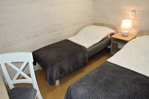 Eine kleine, einfache Unterkunft mit zwei Betten, einem weißen Stuhl und einem Nachttisch mit Lampe.