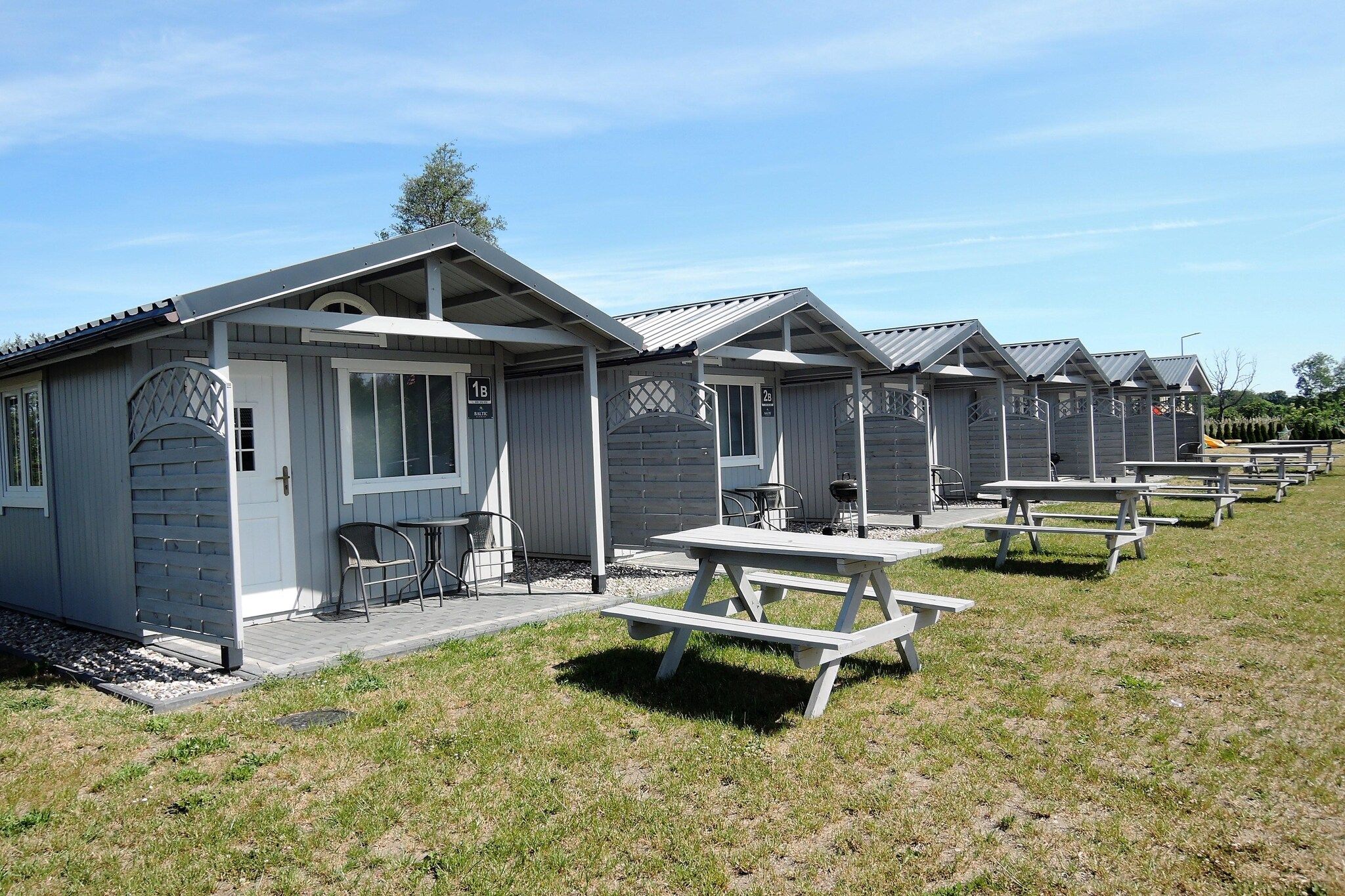 Een rij bungalows met picknicktafels, elk met een klein terrasje en een raam.