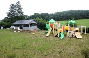 Explore the outdoor play area with slides and climbing elements, surrounded by a grassy field and trees.