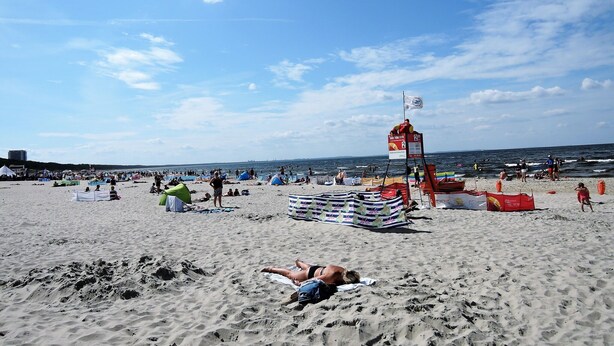 A beach with a lifeguard tower, umbrellas, and beachgoers.