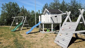 A playground with a slide, climbing wall, and a small wooden house.