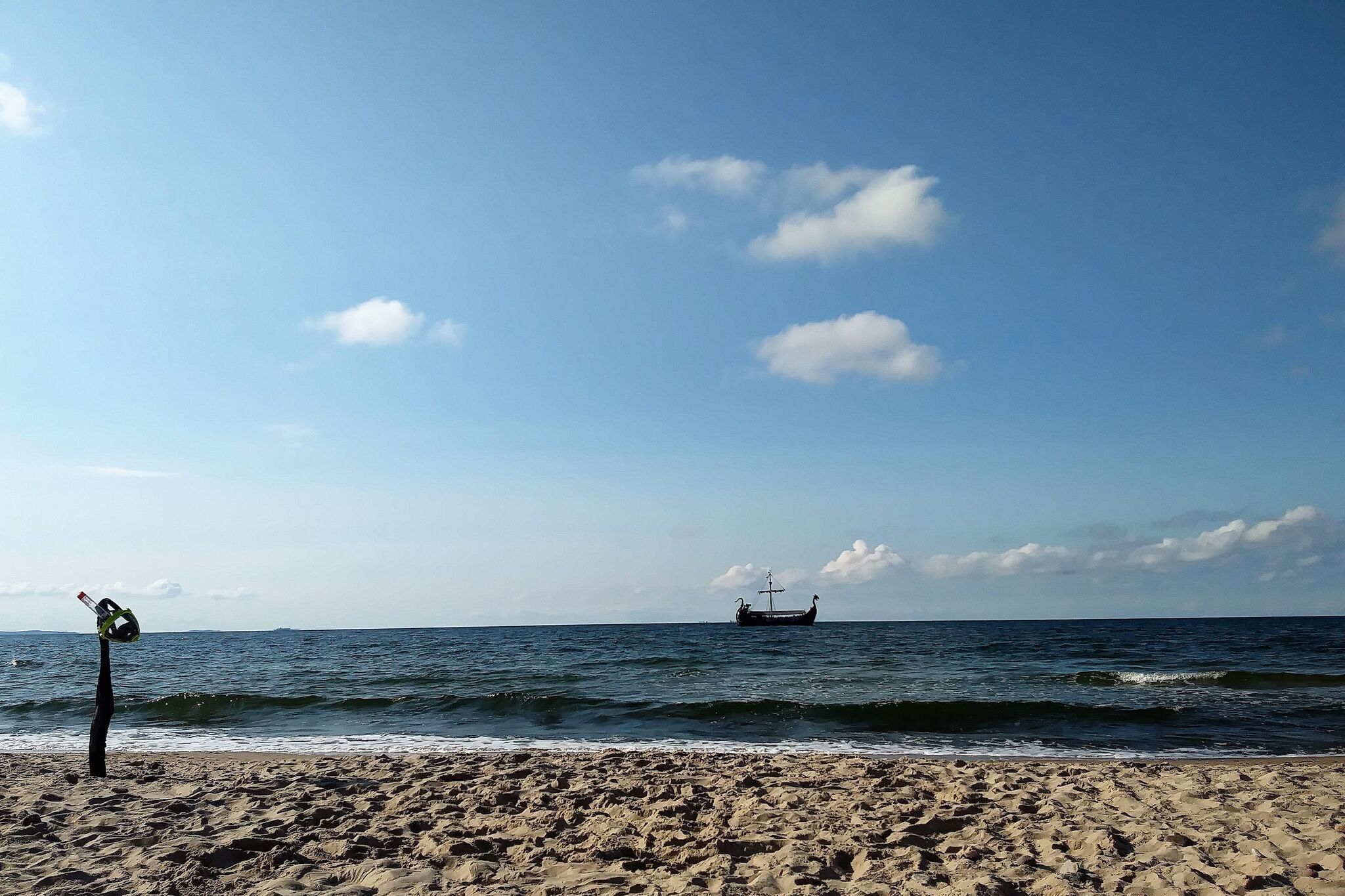 A beach with a ship in the distance and a lifebuoy on the sand.