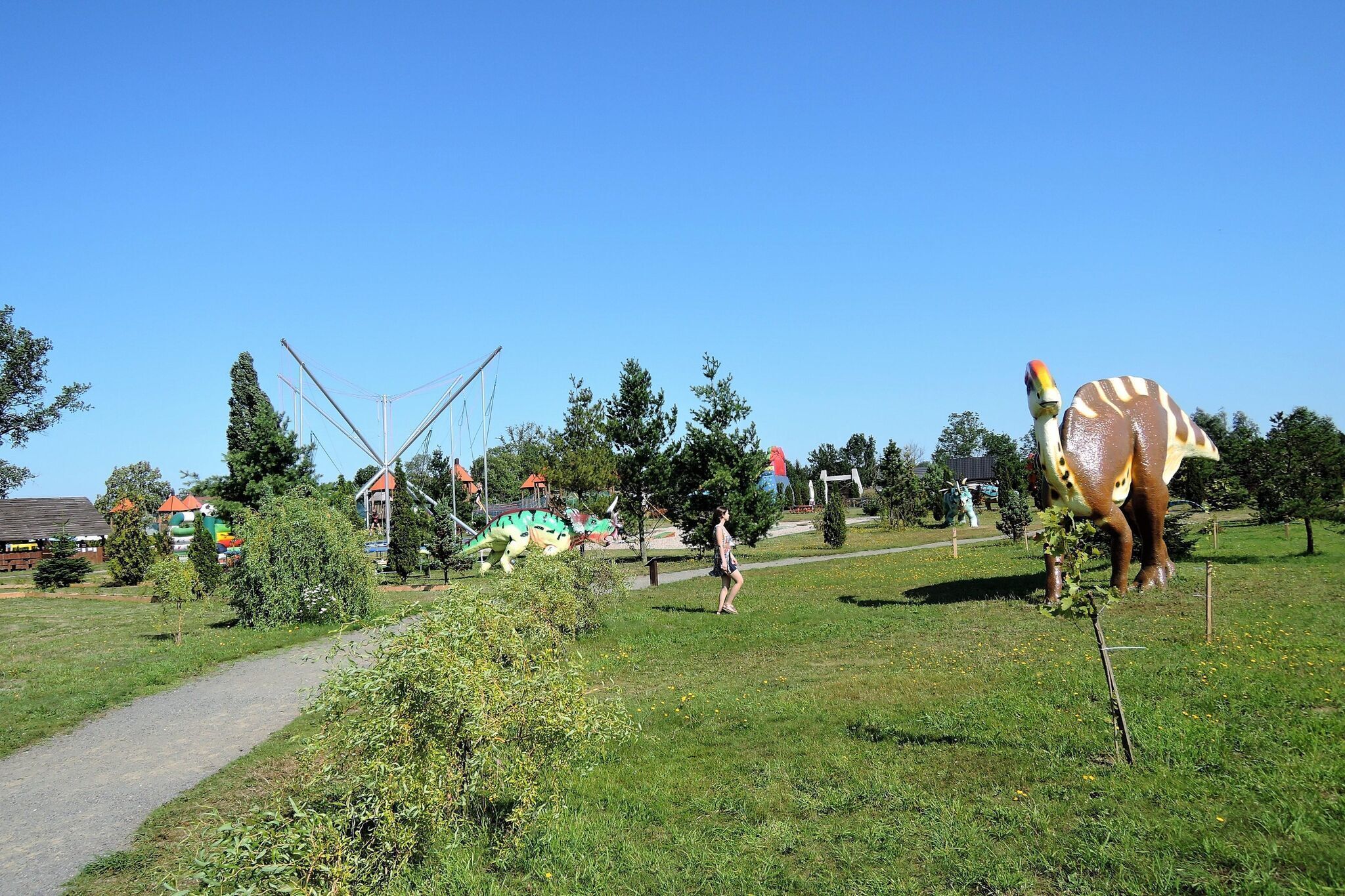 Un parc avec une grande sculpture de dinosaure, un sentier et quelques arbres.