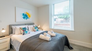 Un dormitorio ordenado con cama, mesitas de noche, ventana con persianas y un cuadro colgado en la pared.