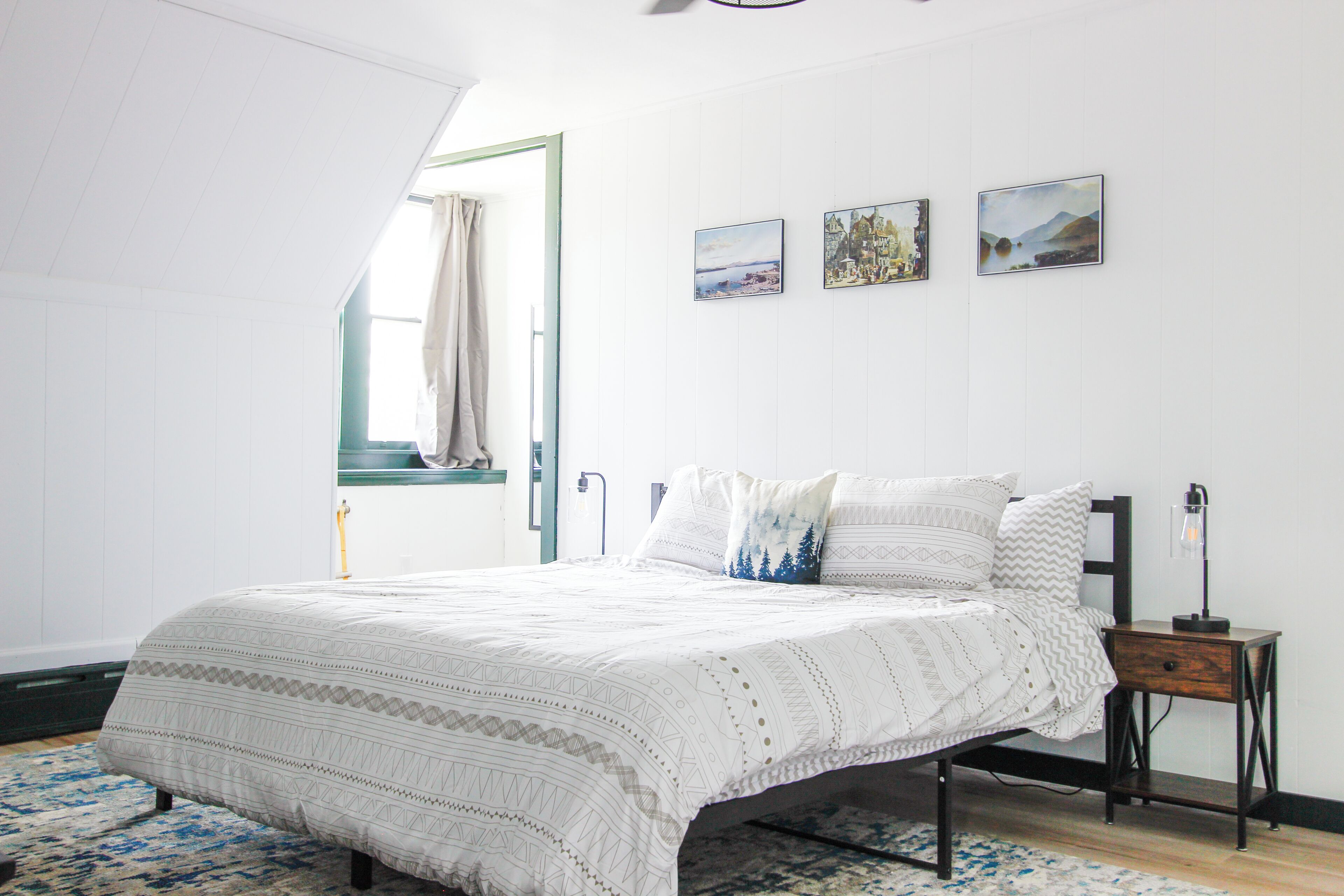 Una camera da letto con un letto, un comodino e una finestra con tende.